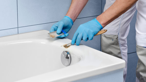 Fotografie für eine Reparatur- oder Bedienungsanleitung. Sauber beleuchtetes, professionelles Bild eines Monteurs beim Reparieren eines Schadens an einer weißen Badewanne.