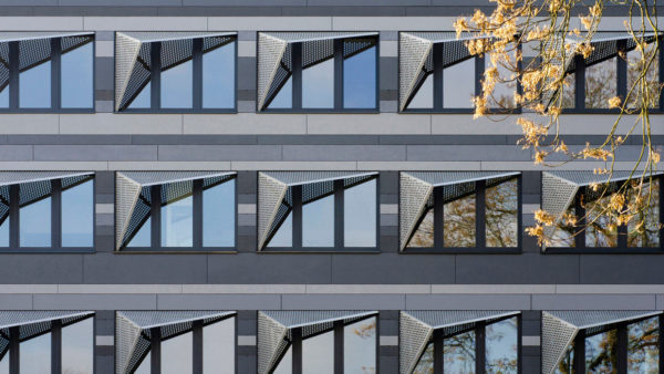 Architekturfotografie: Eine neugestaltete Fassadenansicht mit symmetrisch angeordneten Fenstern und auffälligem Sonnenschutz aus Edelstahl-Lochblechen.